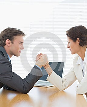 Business couple arm wrestling at office desk