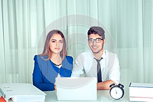 Business couple in office behind laptop looking at you camera happy smiling