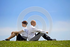 Business couple sitting back to back on grass
