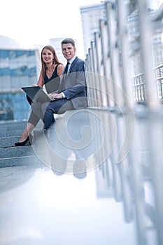 Business couple sitting on steps near office building.
