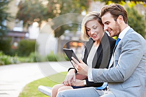 Business Couple Using Digital Tablet On Park Bench