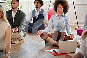 Business coworkers meditating at work, sitting on the floor with legs crossed and eyes closed. modern, casual, business, meditatio