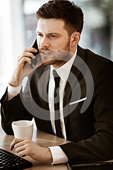 Business crisis concept. Young businessman sitting at the office table busy talking on a cell phone resolving a very