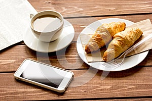 Business cup of coffee with croisant and phone on desk