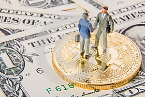 Business deal or agreement and success concept. Two miniature businessmen shaking hands while standing on bitcoin cryptocurrency a