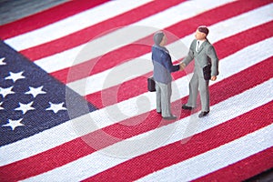 Business deal or agreement and success concept. Two miniature businessmen shaking hands while standing on USA american flag backgr