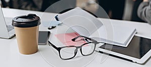 Business desk with a notebook, glasses, pen and tablet on white table