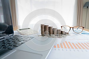 Business documents on table with laptop  and coin stacks and graph financial diagram