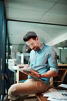 Business, he does it digitally. Shot of a young businessman using a digital tablet in a modern office.