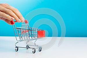 Business and e-commerce concept. Close-up of hand using fingers pushing an empty mini shopping trolley while standing over a blue