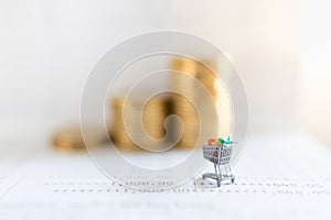 Business E-Commerce and Money Concept. Close up of shopping cart or trolley miniature figure on bank passbook with stack of coins