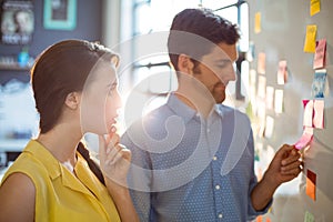 Business executive and co-worker looking at sticky notes on whiteboard