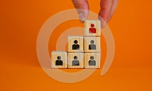 Business executive stacking wooden cubes with people icons on them in a pyramid shape in a conceptual image. Beautiful orange