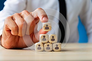 Business executive stacking wooden dices  with people icons on them in a pyramid shape