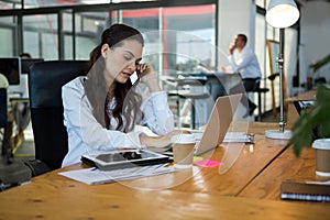 Business executive talking on mobile phone while using laptop at desk