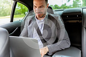 Business executive working on laptop in car during morning commute
