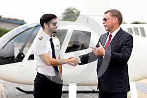 Business executives man in suits shaking hands with helicopter Commercial pilot in uniform near helicopter