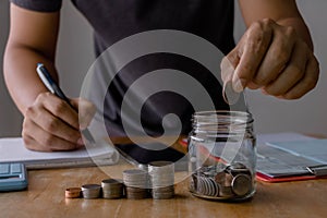 Business finance accounting investment saving money concept. Man hand holding coins putting in jug glass with coins stack step