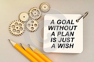 On the table are gears, pencils and a notebook with the inscription - A Goal Without a Plan Is Just a Wish