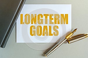 On the table are a notebook, a pen and a business card with the inscription - LONGTERM GOALS photo