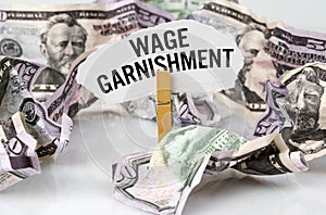 There are dollars on the table and there is a clothespin with paper on which it is written - WAGE GARNISHMENT photo