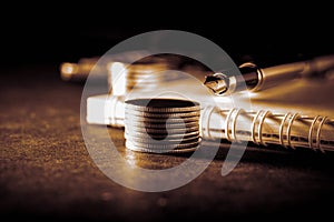 Business, finance or investment concept. Coins in front of cheque book or note book and fountain pen, calculator. Dark toned backg