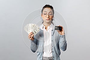 Business, finance and investment concept. Thoughtful indecisive cute asian girl look tempting at cash dollars, holding