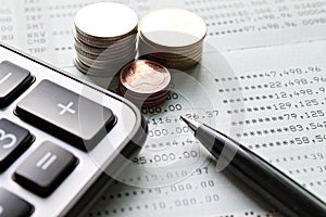 Coin stacks, calculator, pen and savings account passbook or financial statement on office desk table