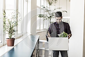 Business, firing and job loss concept. Sad fired indian male office worker holding box of his personal stuff