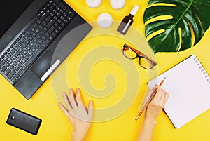 Business flatlay with laptop, mobile phone, glasses, philodendron leaf, candles, cream and other accessories