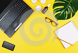 Business flatlay with laptop, mobile phone, glasses, philodendron leaf, candles, cream, pen and notebook.