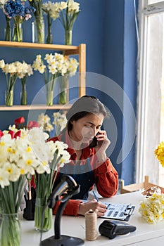 Business and floristry concept. happy smiling florist woman taking order on cellphone working at her flower shop