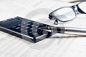 Business fountain pen, calculator and glasses on financial chart