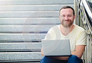Business and freedom. Happy modern businessman, man with a beard behind a laptop in nature sits smiling on the steps and running.