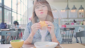 Business freelance Asian woman eating bread and drinking warm cup of coffee while sitting on table in cafe.