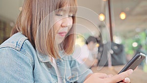 Business freelance Asian woman using smartphone for talking, reading and texting while sitting on table in cafe.