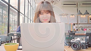 Business freelance Asian woman working, doing projects on laptop and drinking warm cup of coffee while sitting on table in cafe.