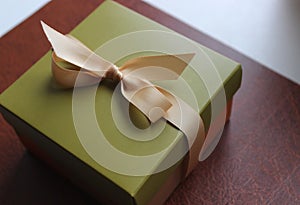 Business gift wrapping in olive tones with an elegant beige ribbon on brown leather