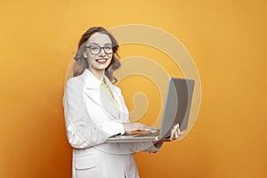 business girl in glasses and suit uses laptop on colored background, female manager works at computer and smiles