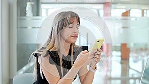 Business girl in the office, sitting at a table with a laptop, working in a smartphone.