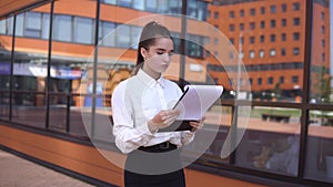 Business girl is walking down the street and looking at documents. 4K