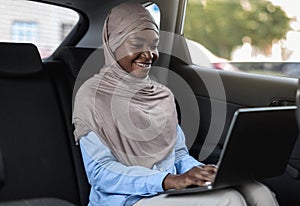 Business On The Go. Black Muslim Businesswoman Working On Laptop In Car