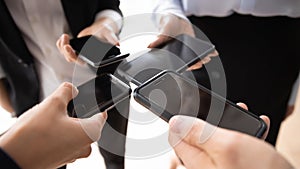 Business group standing in circle, holding similar mobile phones together