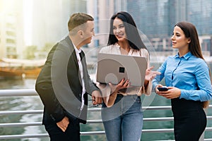 Business group watching and discussing project presentation outdoors. Two Men and woman in office suits standing outside, using