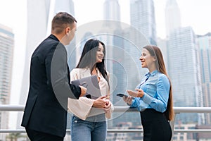 Business group watching and discussing project presentation outdoors. Two Men and woman in office suits standing outside, using