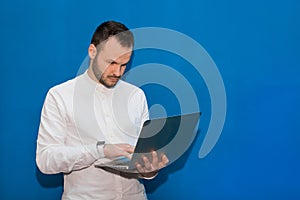 Business guy stylish businessman of European appearance corresponds in a laptop on a blue background photo