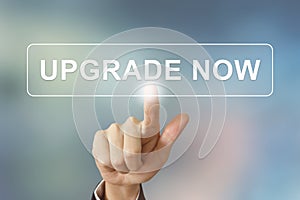 Business hand clicking upgrade now button on blurred background photo