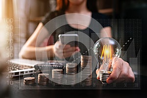 Business hand holding lightbulb with using laptop computer and money stack in office. idea saving energy and accounting finance