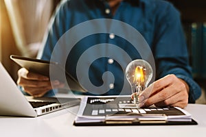 Business hand holding lightbulb with using laptop computer and money stack in office. idea saving energy and accounting finance