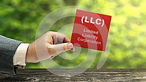 Business hand holding a note with LLC text, the acronym of Limited Liability Company